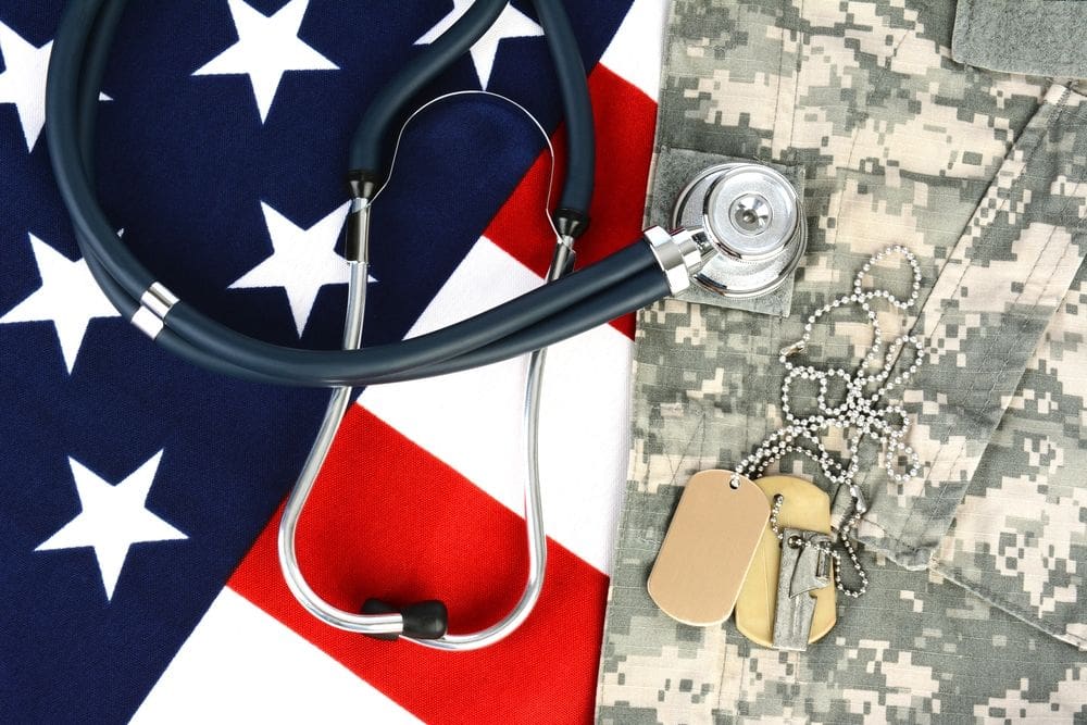 32f57572f5b215c2282ee858a879981c203eb4d2-1000x667.jpg Stethoscope and military dog tags placed on a camouflage uniform, with an American flag background, symbolizing the service of an African American vet.