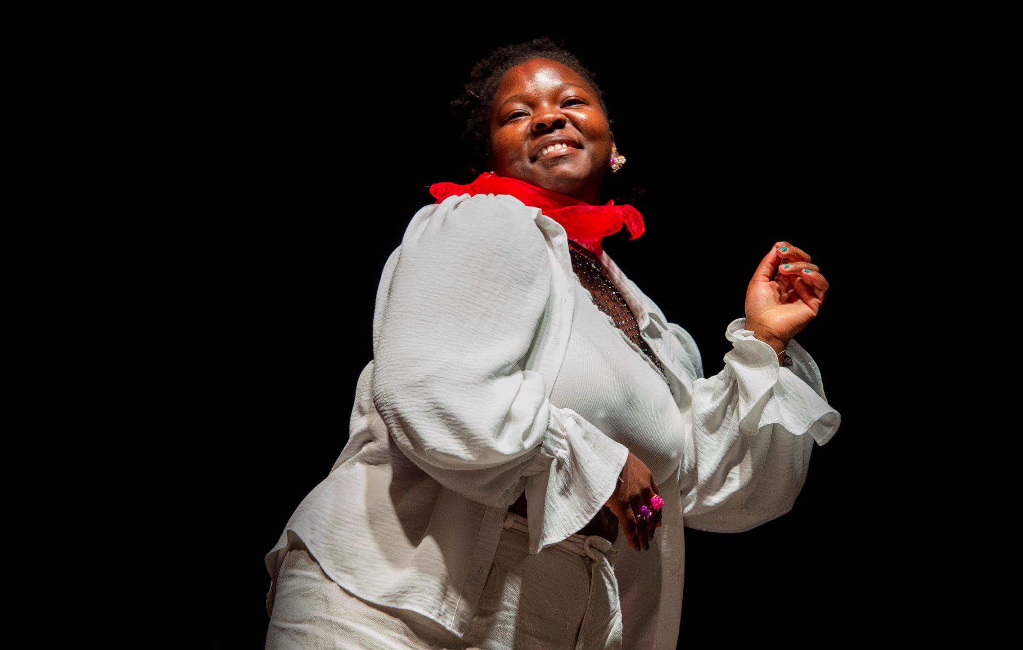 Kokoroko-2000-x-1270.jpg A person dressed in white with a red scarf poses confidently against a black background, reminiscent of the vibrant style seen in KOKOROKO's 2023 Australian tour.