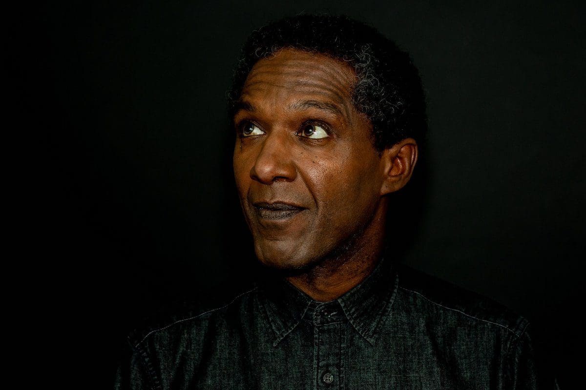 Lemn-Sissay_credit-JamieMacMillan-1-min.jpg A person with short, curly hair and dark eyes is looking upward, wearing a dark-colored button-up shirt against a dark background—an image that captures the contemplative spirit often celebrated during Black History Month.