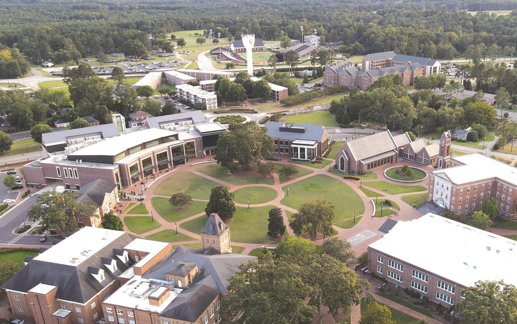 WDJI_0088-1.jpg Aerial view of Duke university campus featuring multiple academic buildings, green spaces, and pathways arranged in an organized layout with a forested area in the background, often explored by visiting scholars or a passionate Spanish professor.