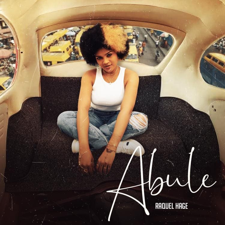 WhatsApp-Image-2022-10-10-at-17.01.33.jpg A person with a half-black, half-blonde afro hairstyle sits with crossed legs in the back of a vehicle on a street. The text "New Single: Abule by Raquel Hage" is displayed in the lower-right corner.