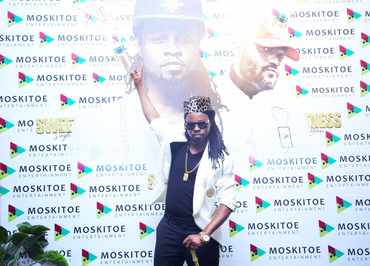 WhatsApp-Image-2022-10-21-at-9.34.03-AM.jpeg A person wearing a crown and sunglasses poses in front of a backdrop featuring images of other individuals, the logo "Moskitoe Entertainment," and a subtle nod to TikTok's aesthetic.