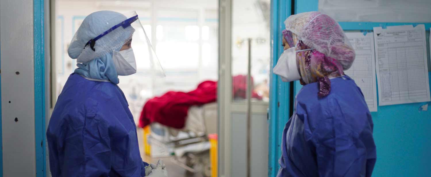 a1-healthcare.jpg Two healthcare workers wearing protective gear talk in a hospital hallway, with a patient on a bed visible in the background, discussing the latest developments in medical and vaccines needed for an upcoming Market Days event.