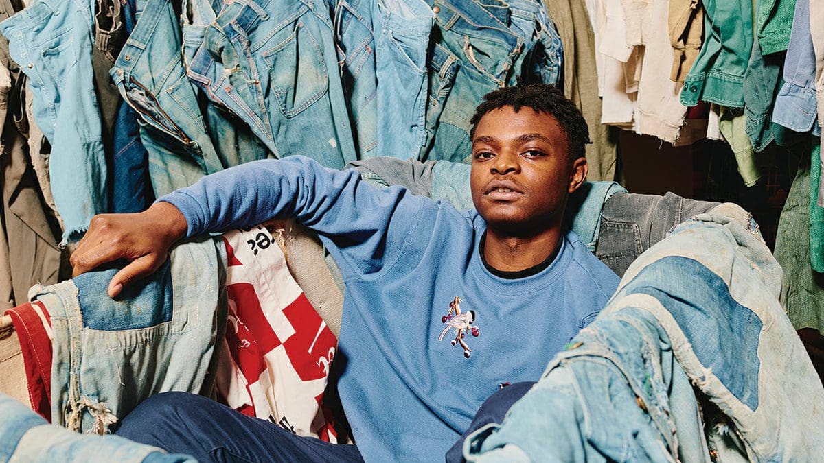 miloe2.jpg A person in a blue sweatshirt sits in a chair surrounded by various jackets and garments, particularly denim, with an expression of relaxed confidence, embodying the effortless cool of What Made Gaps.
