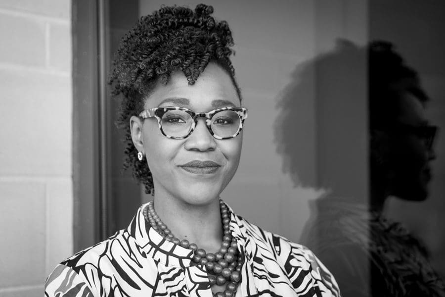 2022-10-31_12-23-01-PMDrGreene_Headshot_MelissaBlackall_-40.jpg Black and white image of a person wearing glasses, patterned clothes, and a beaded necklace, standing next to a reflective surface. They have short, curly hair styled upwards. This portrait celebrates Nikki A. Greene, the renowned Artwork Historian featured in our Visiting Lecture Series.