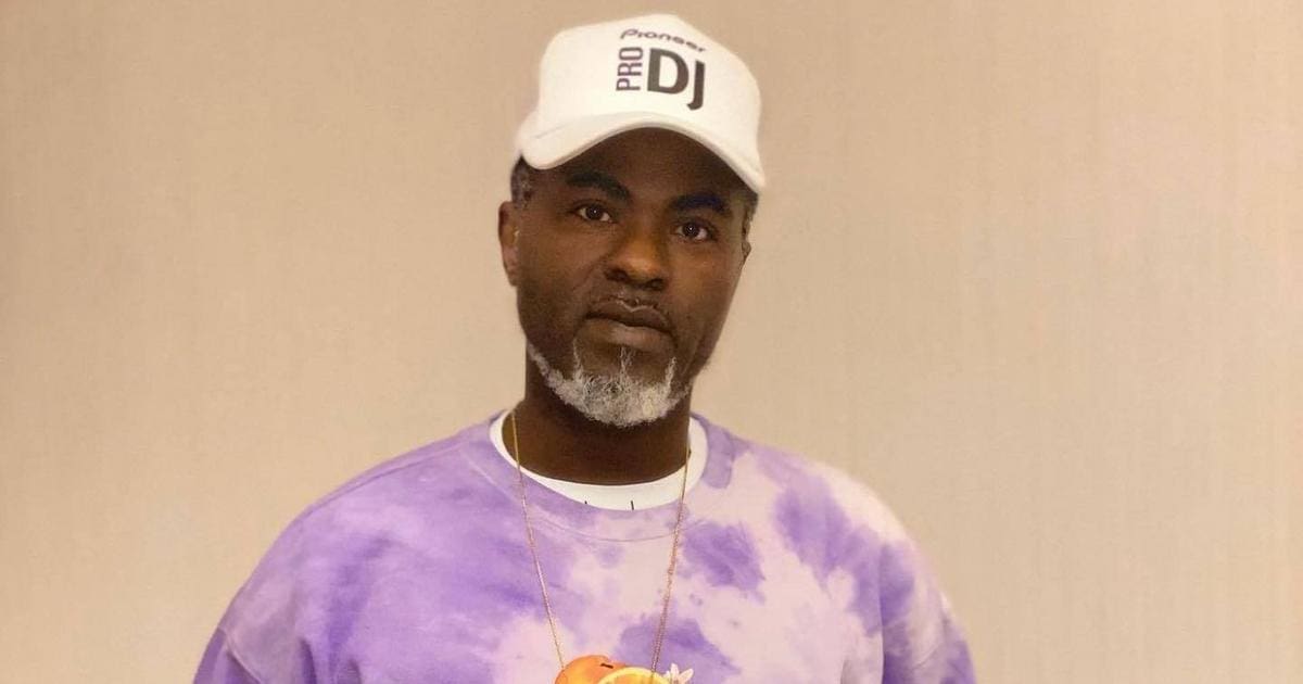 H81ktkpTURBXy9kY2E3YmNhMTQxYmEwMWU1MjgyNjE2NzRkN2U3ZDU5My5qcGeSlQMAM80FoM0DKpMFzQSwzQJ2.jpeg A person with a grey beard and mustache wearing a white baseball cap labeled "Pioneer DJ," a gold chain, and a purple tie-dye shirt stands in front of a neutral background. This Nigerian disc jockey, known as DJ Blackk Beat, brings the vibrant energy of Afrobeats to every performance.