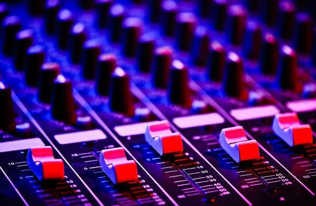 Music.jpg Close-up of an audio mixing console with sliders and knobs, lit by purple and red lighting, setting the stage for Moradeyo, the full entertainer.