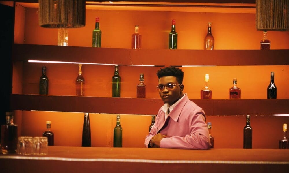 maxresdefault-22-1000x600.jpeg A person dressed in a purple jacket stands behind a bar with various bottles on shelves in the background under warm lighting, featured prominently in our new video by Soundz.