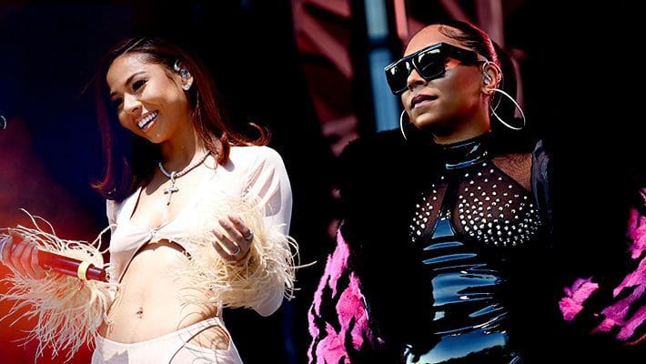 rnb-grid-uproxx-1.jpg Two women performing on stage, one wearing a white outfit with feather details and holding a microphone, the other in a black studded outfit with large sunglasses and a black and pink jacket. Their soulful harmonies are reminiscent of Ashanti's classics, delivering some of the greatest new R&B songs.