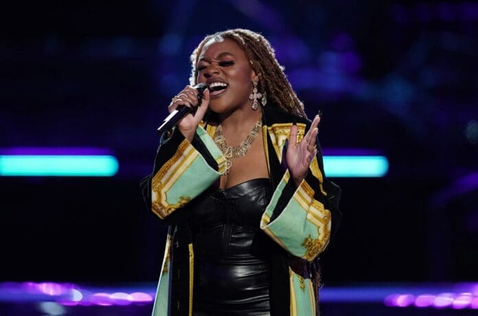 Libianca-2021-billboard-1548.jpg A woman with long braided hair sings passionately into a microphone on stage. She wears a black strapless dress and a decorative overcoat, with a dark background and purple-blue lighting, delivering an electrifying Afrobeats performance that's worthy of Billboard acclaim.