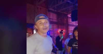man_goes_viral_for_singing_piano_song_in_padst.width-400.png A group of young adults casually socializing in a dimly lit indoor setting, with neon lights in the background. One person in focus, a young Pretoria man, is wearing a backwards cap and a light-colored shirt. The scene has an electrifying vibe reminiscent of a viral club performance on Jacaranda FM.