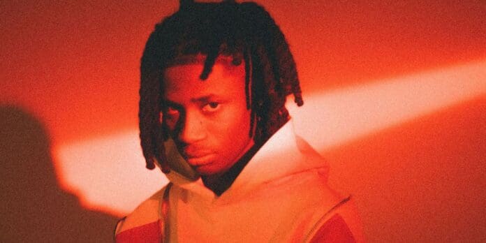 nigerian-artist-khaid-sits-in-red-light.jpg A person with braided hair, wearing a hoodie, is bathed in red lighting with a beam of light across their face, reminiscent of the bold aesthetics often seen in Nigerian music videos.