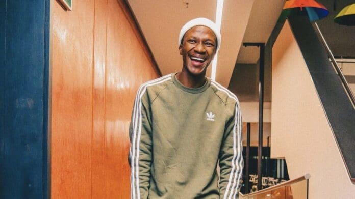 A man in a green sweater is smiling in front of a staircase at amapiano innovator Mdu aka TRP's donation. A man in a green sweater is smiling in front of a staircase at amapiano innovator Mdu aka TRP's donation.