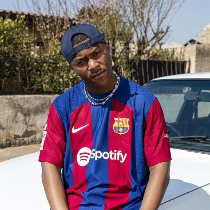 A man in a Barcelona jersey sitting on a car. A man in a Barcelona jersey sitting on a car.