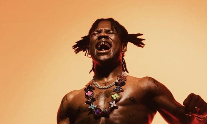 A man with dreadlocks is singing in front of an orange background at the O2 Arena in London. A man with dreadlocks is singing in front of an orange background at the O2 Arena in London.