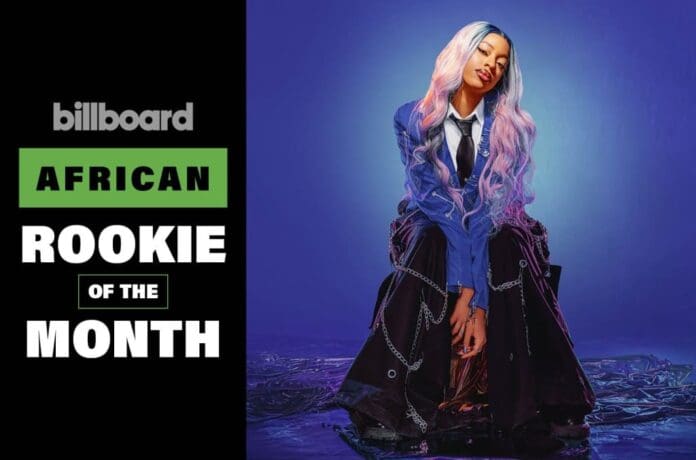 Qing-Madi-cr-02-Kelechi-Amadi-Obi-African-Rookie-of-the-Month-billboard-1548.jpg Qing Madi, with her long, multicolored hair, sits gracefully on the floor in a blue jacket and black skirt. Text reads "Billboard African Rookie of the Month," celebrating her as a rising star blending Afropop influences with smooth R&B melodies.