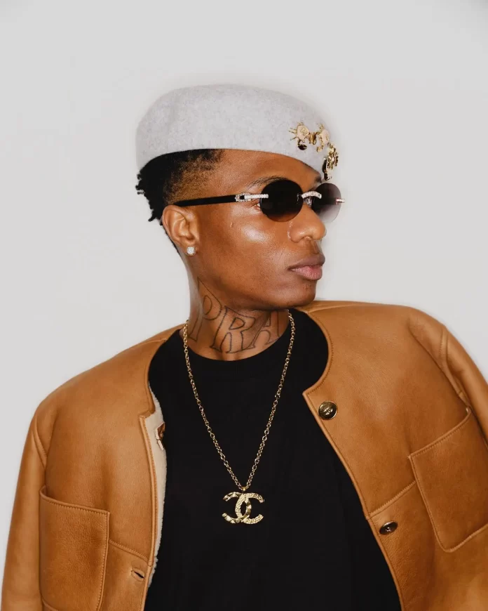 Wizkid-Ayo-OlorisupergalMedia.webp.webp Donning sunglasses and a light hat with embellishments, the individual channels Wizkid's effortless style in a brown jacket over a black shirt and gold chain necklace, setting the scene for DJ Henry to drop an exclusive, unreleased song.