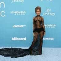 67f0229b87778.image_.jpg Person in a sheer, black patterned gown with a long train stands on a blue carpet adorned with Spotify logos, showcasing the latest trends from the world of South African music.