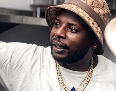 Person wearing a Gucci bucket hat, white t-shirt, and gold chain, looking to the side.