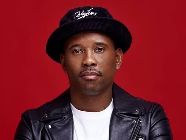 Person wearing a black hat and leather jacket against a red background.