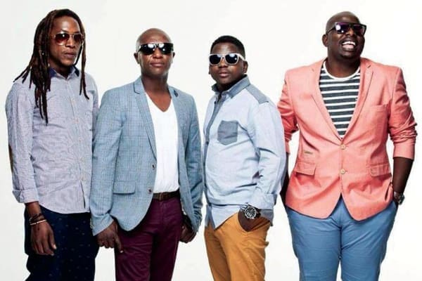 Four men stand side by side against a plain background, each wearing sunglasses and smart-casual clothing in different colors and styles.