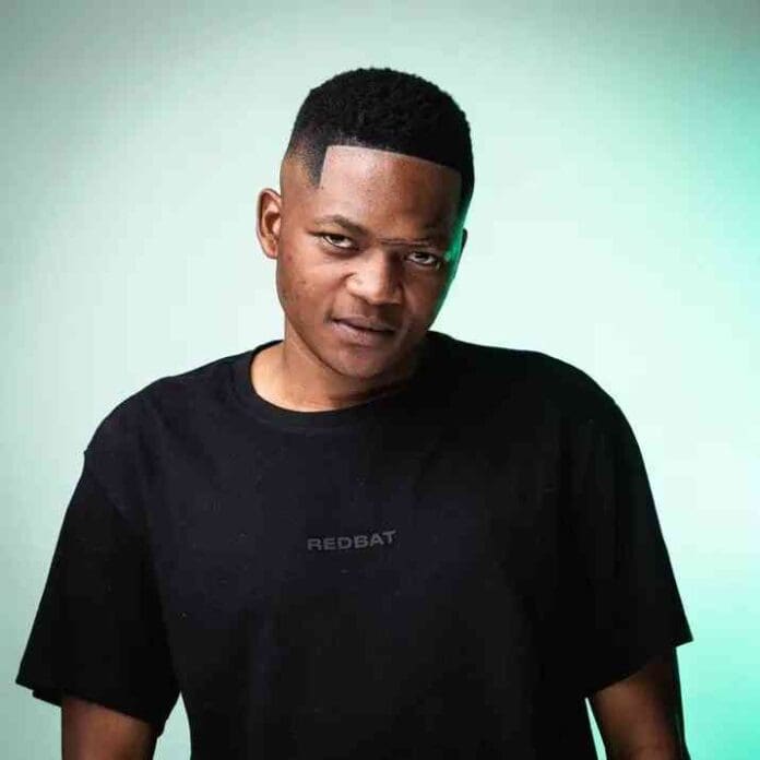 img_1_1744864391607.jpg A man with short hair wearing a black "REDBAT" t-shirt stands against a light gradient background, looking toward the camera, as if ready to drop beats for Kap Sessions Vol. 6 with Vyno Keys.