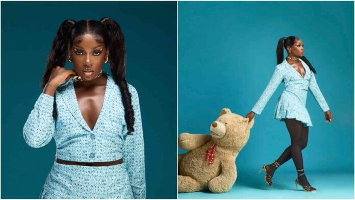 j3seiif7IkVwNlLnwyq2XX76QjkoIoPVNsmPKoy0.jpg Modola, in a light blue outfit with pigtails, poses against a turquoise background beside a large teddy bear. She exudes style and rhythm akin to Afrobeats, wearing black tights and high-heeled sandals with an effortless charm that speaks volumes without saying a word.