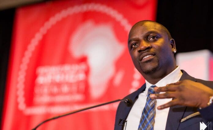00390853fb6b02211f96e3a8837bcee7de35245aarc614x376w1200.jpg A man in a suit speaks at a podium in front of a red banner featuring a white map of Africa, highlighting the influence of Nigerians in the rise of Afrobeats.