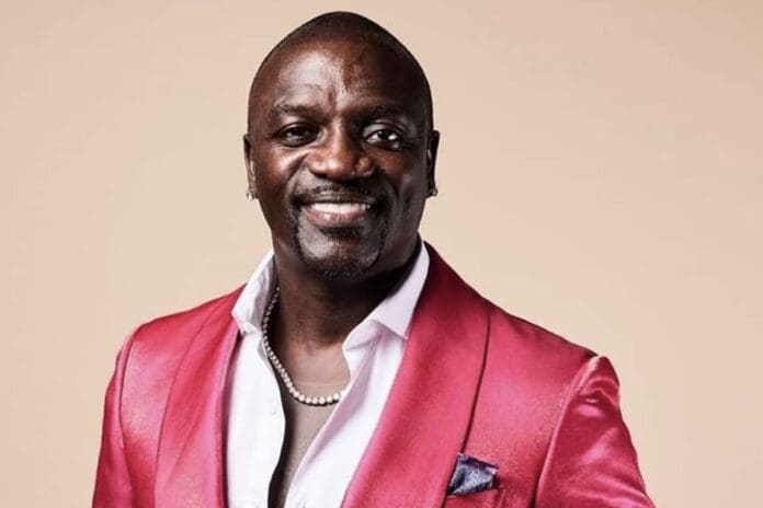 Akon.-Photo-Revolt-TV.jpg A man wearing a shiny pink suit jacket, white shirt, and pearl necklace smiles at the camera against a beige background, channeling Wizkid’s signature style seen in Guardian Nigeria News.