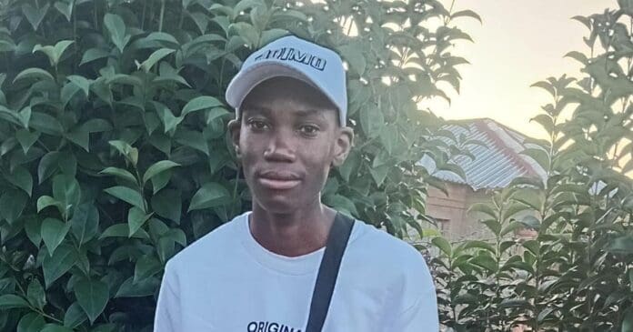 Amapiano.jpg A young Potch DJ wearing a white cap, white T-shirt, and black shoulder bag stands in front of green foliage and a building with a tin roof at sunset, capturing the vibe of someone ready to claim the Best Amapiano Single award.