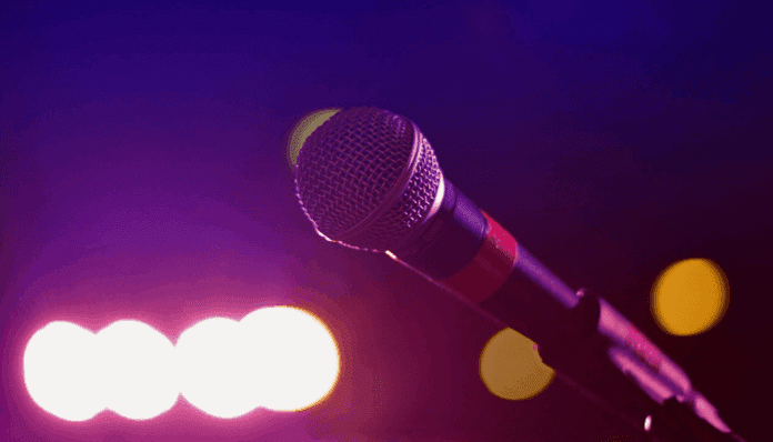 Nigerias-music-industry-1.png A close-up of a microphone on a stand with blurred stage lights in the background, capturing the vibrant spirit of African music and the dynamic energy of performing arts Nigeria.