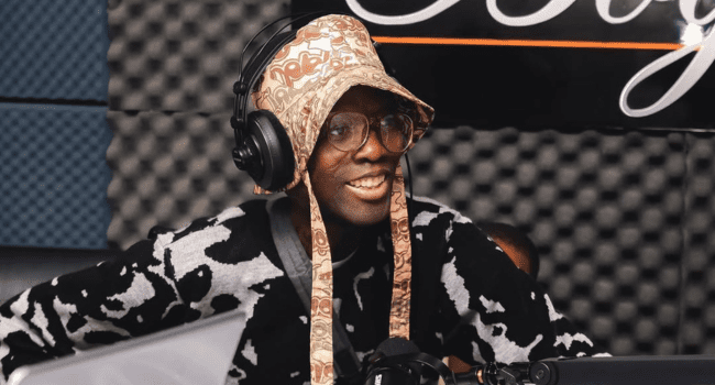 Rashid.png A person wearing glasses, headphones, and a patterned hat sits in a soundproof recording studio with a microphone—looking like Rashid Kay during an SA Hip Hop session or prepping for the Metro FM Awards.