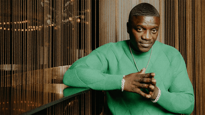 image-1.png A man in a green sweater sits at a bar with his hands clasped, looking towards the camera. Gold beaded curtains hang in the background, creating an atmosphere reminiscent of Akon’s signature Afrobeats music videos.