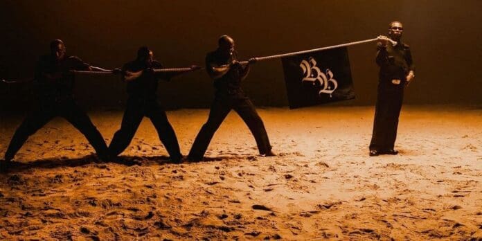 image.jpg Four men on a sandy surface engage in a tug-of-war with a rope; three pull on one side while one stands alone holding a black flag with stylized white letters, reminiscent of the bold visuals often seen in Burna Boy’s new single promoted by OkayAfrica.